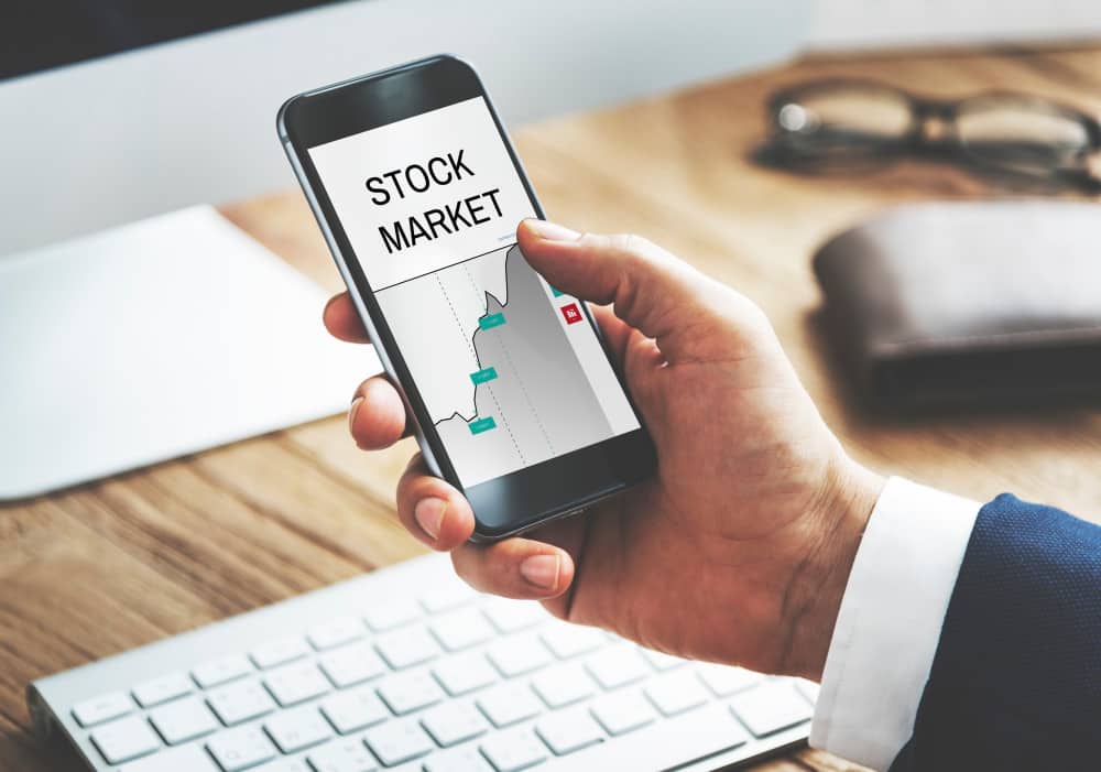 Un investisseur en costume utilise son smartphone pour obtenir un accès aux marchés boursiers et consulter des graphiques financiers en temps réel.