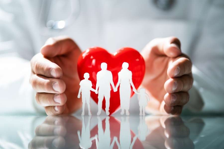 Des mains protègent une figurine de famille en papier et un cœur rouge pour symboliser l'assurance santé.