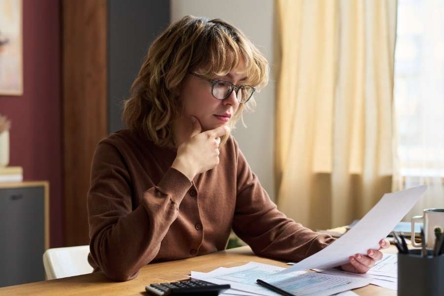 Une femme examine un document financier pour sécuriser ses comptes bancaires à domicile.